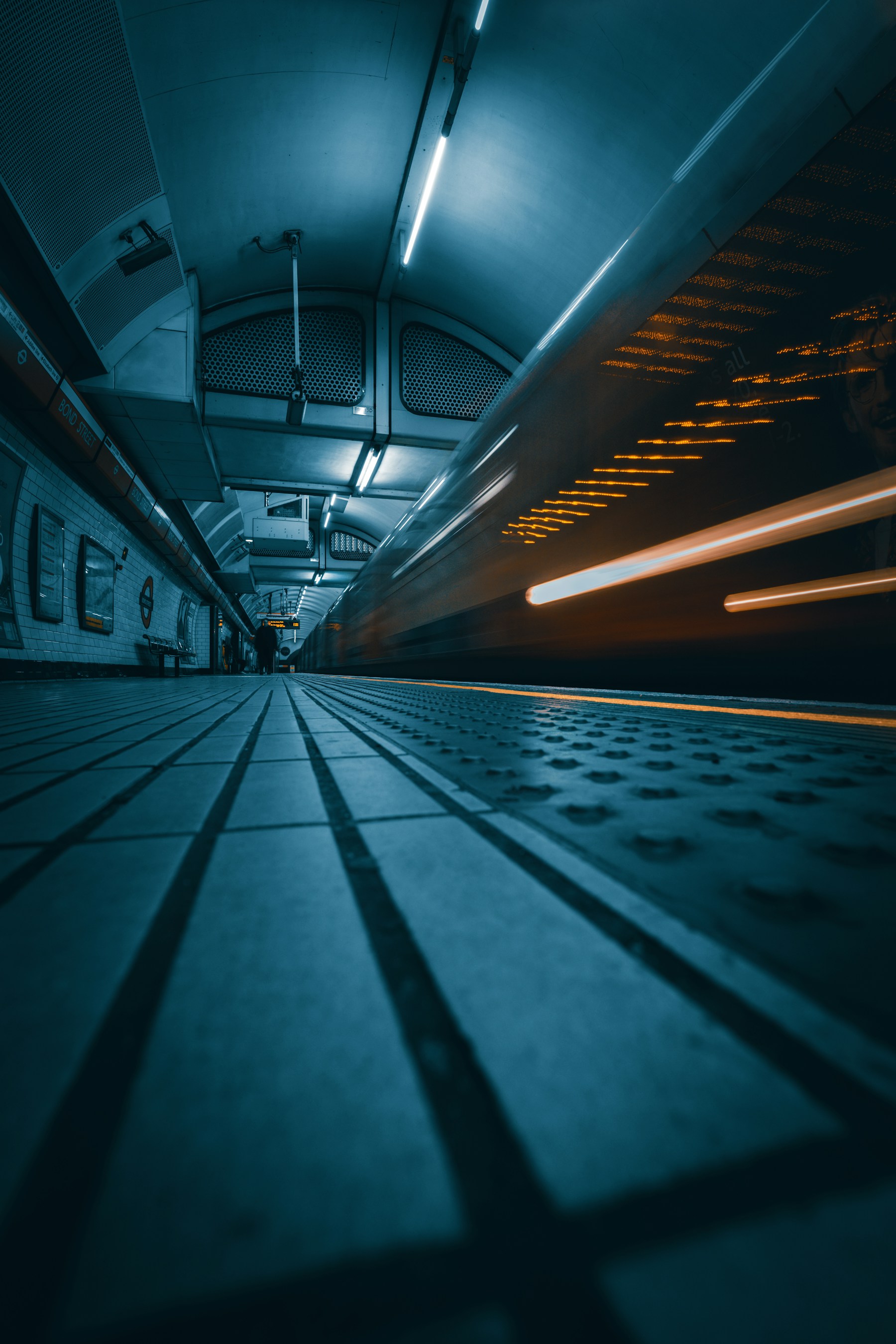A train moves through a blue-lit London Underground station